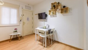 A small, well-lit room with a white table and chairs, a television mounted on the wall, and a door with a window. - apartamento en lavapies de alquiler temporal (Madrid)