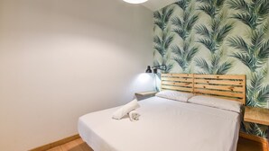 A neatly made bed with a wooden headboard, a white pillow, and a rolled towel on the bed. - apartamento en lavapies de alquiler temporal (Madrid)