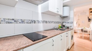 A modern kitchen with white cabinets, a granite countertop, a built-in stove, a washing machine, and a tiled backsplash. - apartamento en lavapies de alquiler temporal (Madrid)