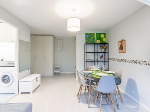 A modern kitchen with white cabinets, a built-in washing machine, and a dining area with a glass table and chairs.