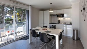 A modern kitchen with white cabinets, a dining table with four chairs, and a large sliding glass door leading to a balcony with outdoor seating. - Les Cyprès by Interhome (Saint Malo)