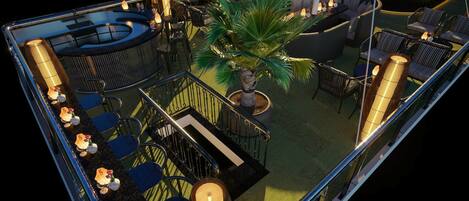 A rooftop bar with a pool, lounge chairs, and a palm tree.