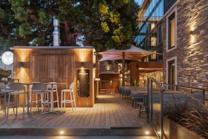 An outdoor patio area with wooden flooring, metal chairs, and tables. There is a stone wall with a sign that reads "COCO CABANA."
