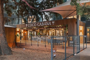 A modern outdoor seating area with a wooden deck, glass railings, and a sign for 'COCO CABANA'.