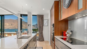A modern kitchen with a large island, stainless steel appliances, and a view of mountains and water. - Chic Central Penthouse & Spa by Staysouth (Queenstown)