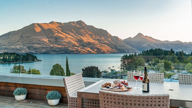 A terrace with a table set for two, overlooking a lake and mountains. - Chic Central Penthouse & Spa by Staysouth (Queenstown)
