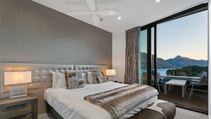 A bedroom with a large bed, a ceiling fan, and a view of the mountains through a large window. - Chic Central Penthouse & Spa by Staysouth (Queenstown)