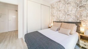 Ett sovrum med en säng, ett nattduksbord, en lampa och en tapet med blommönster.