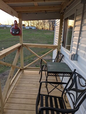 A covered outdoor deck with a wooden floor, metal chairs, and a table. - Cowboy Cottage (Florence)