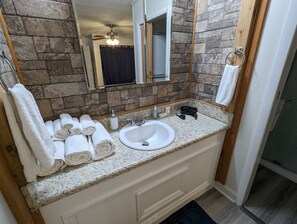 A bathroom with a granite countertop, white sink, and a mirror above it. There are towels stacked on the left side and a bottle of hand soap on the countertop. - Cowboy Cottage (Florence)