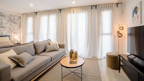 Ett modernt vardagsrum med en soffa, ett soffbord, en tv och gardiner.