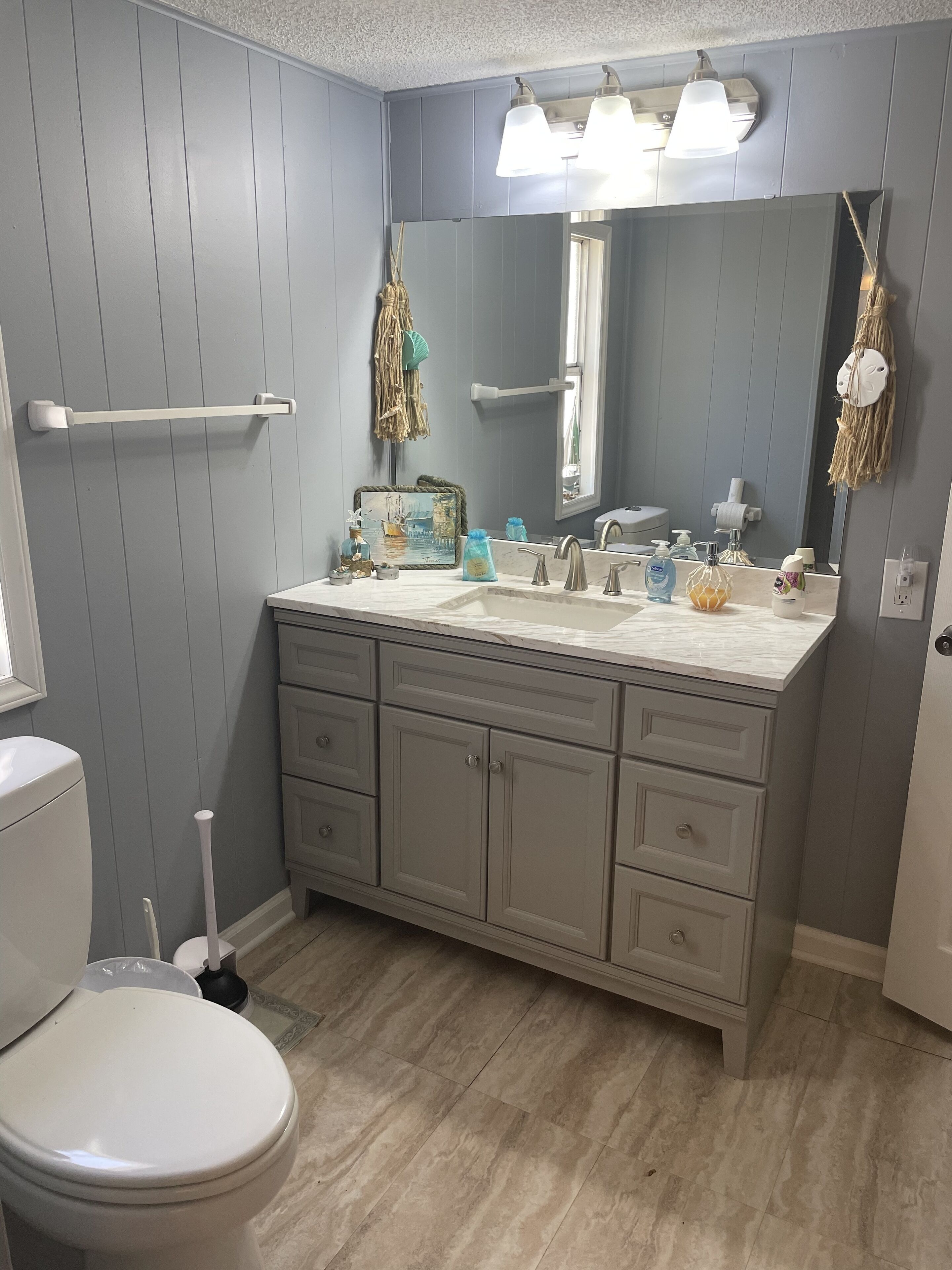 Ein Badezimmer mit Toilette, Waschtisch inklusive Spiegel und Waschbecken. Auf dem Waschbecken liegen Toilettenartikel, und ein Handtuchhalter ist zu sehen.