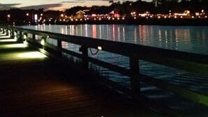 Vista nocturna d'un passeig marítim amb una passera de fusta i baranes.