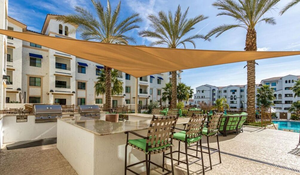 An outdoor bar area with a pool, bar stools, and a grill.