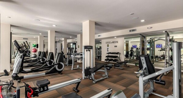 A modern gym with cardio machines, weightlifting equipment, and a mirrored wall.
