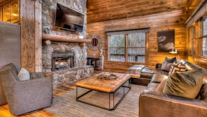 A cozy cabin interior with a stone fireplace, leather furniture, and a television mounted on the wall. - Tranquility Ranch - Hot Tub | Pool Table | Fire Pit in Private Yard (Mineral Bluff)