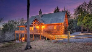 A log cabin with a porch and a stone chimney, surrounded by trees. - Tranquility Ranch - Hot Tub | Pool Table | Fire Pit in Private Yard (Mineral Bluff)