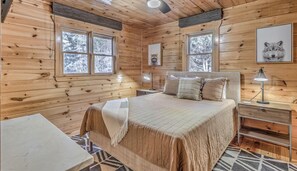 A cozy log cabin bedroom with a large bed, two bedside tables, a desk, and a chair. - Tranquility Ranch - Hot Tub | Pool Table | Fire Pit in Private Yard (Mineral Bluff)