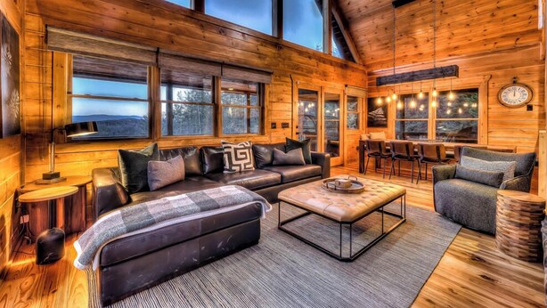 A cozy cabin interior with a leather sofa, a coffee table, and a dining area with chairs. - Tranquility Ranch - Hot Tub | Pool Table | Fire Pit in Private Yard (Mineral Bluff)