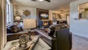 A cozy living room with a fireplace, leather sofas, a coffee table, and a ceiling fan. - Farmhouse Cottage - Close to Tanger Outlets and Pigeon Forge! (Sevierville)