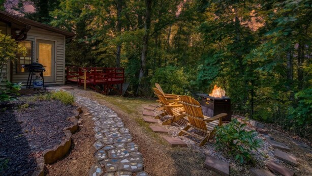 A wooden deck with Adirondack chairs, a fire pit, and a stone pathway leading to a cabin. - Farmhouse Cottage - Close to Tanger Outlets and Pigeon Forge! (Sevierville)