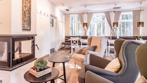A modern living room with a fireplace, comfortable seating, and large windows offering a view of trees.