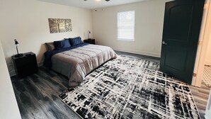 Ein Schlafzimmer mit einem Bett, Deckenventilator, Fenster, Tür und einem Nachttisch mit Lampe.