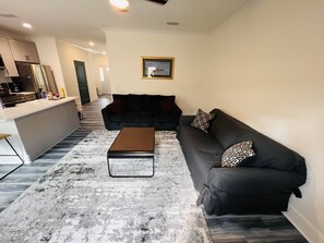 Una sala de estar moderna con un sofá negro, una mesa de centro de madera y una alfombra estampada.
