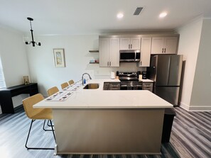 Una cocina moderna con una isla central, electrodomésticos de acero inoxidable y una zona de comedor con sillas.