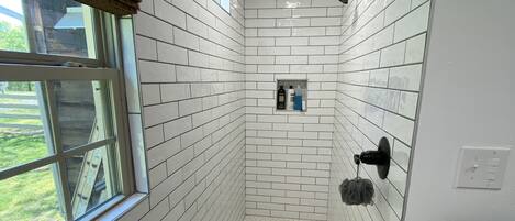 A bathroom with white hexagonal tiles, a shower area, a window with a view, and a towel rack.