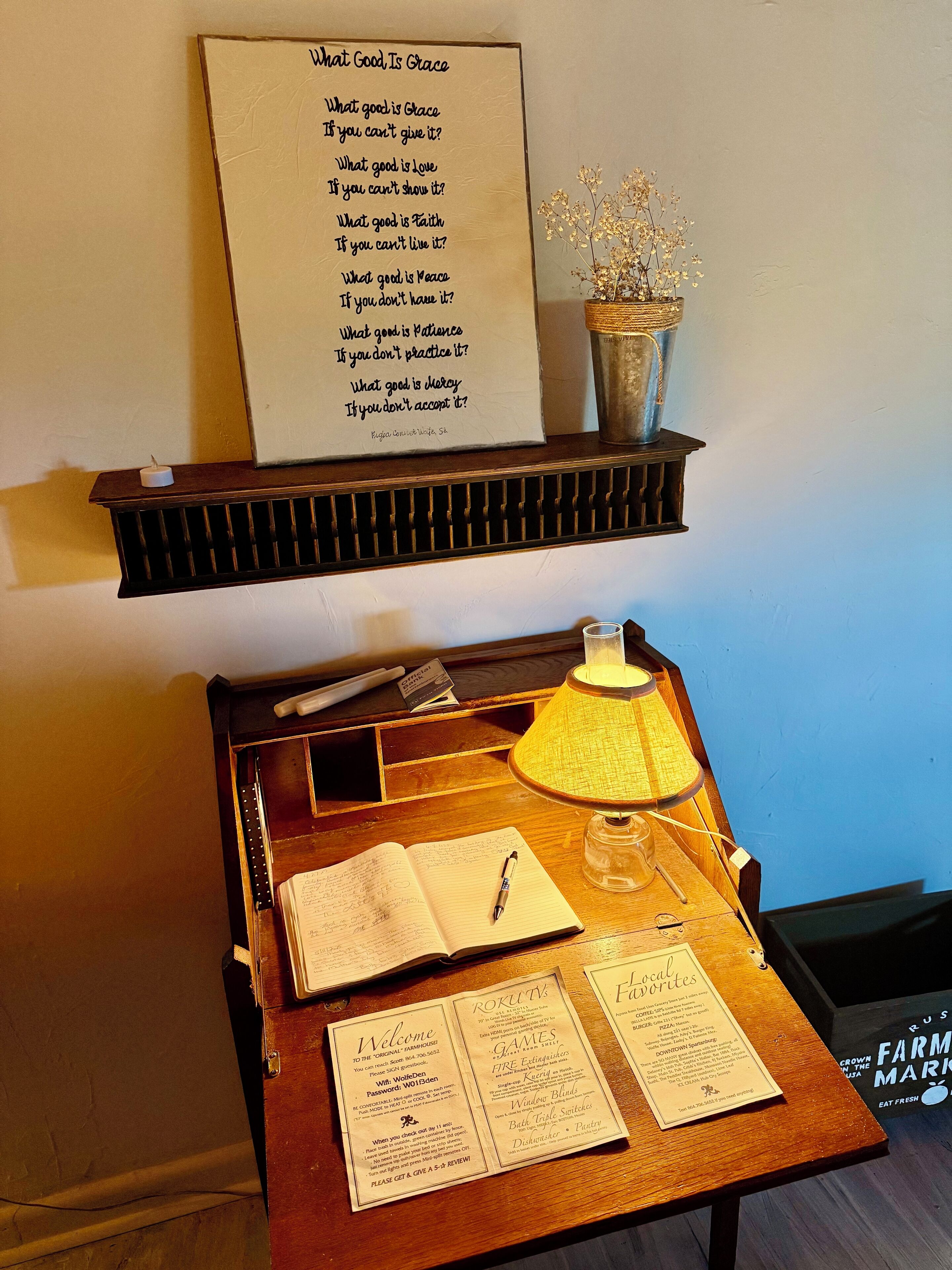 A wooden desk with a lamp, a notepad, and a pen. Above the desk, there is a framed quote on the wall.
