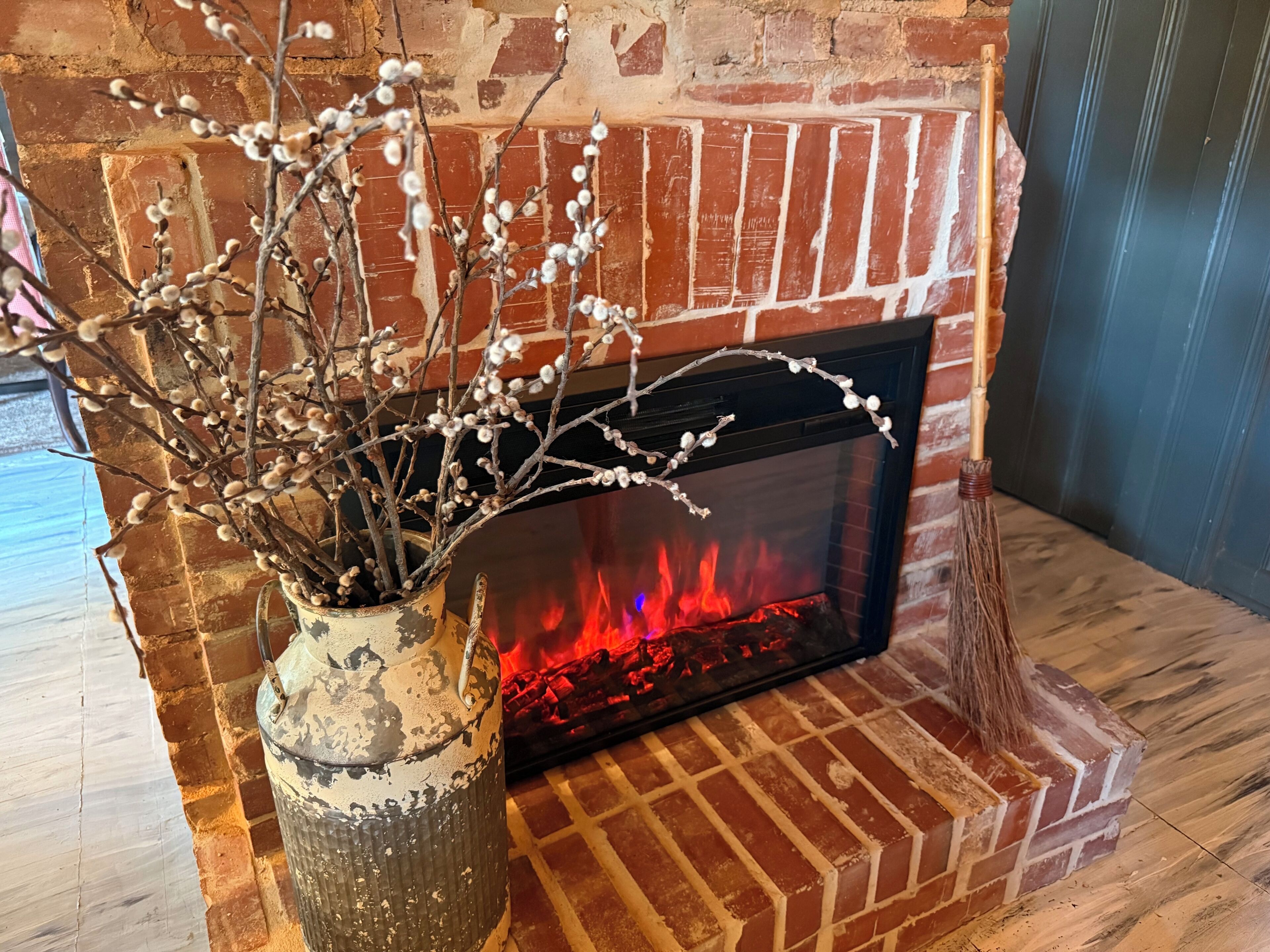 A brick fireplace with a vase of branches and berries.