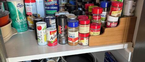 Uma despensa de cozinha repleta de diversos alimentos e temperos, incluindo especiarias, sprays de cozinha e uma panela de cozimento lento.