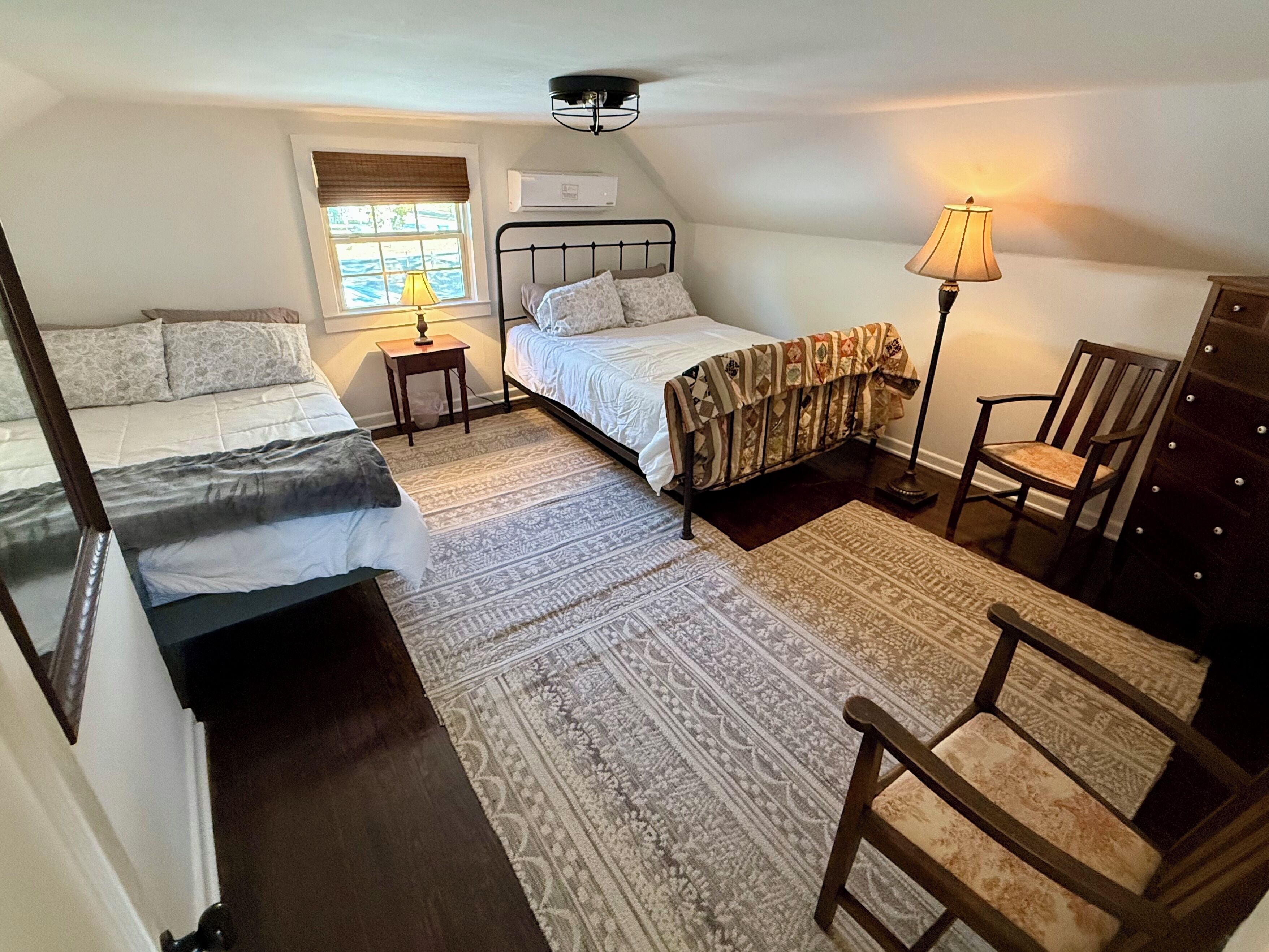A bedroom with two beds, a window with a view, a lamp, a chair, and a dresser.