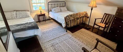A bedroom with two beds, a window with a view, a lamp, a chair, and a dresser.