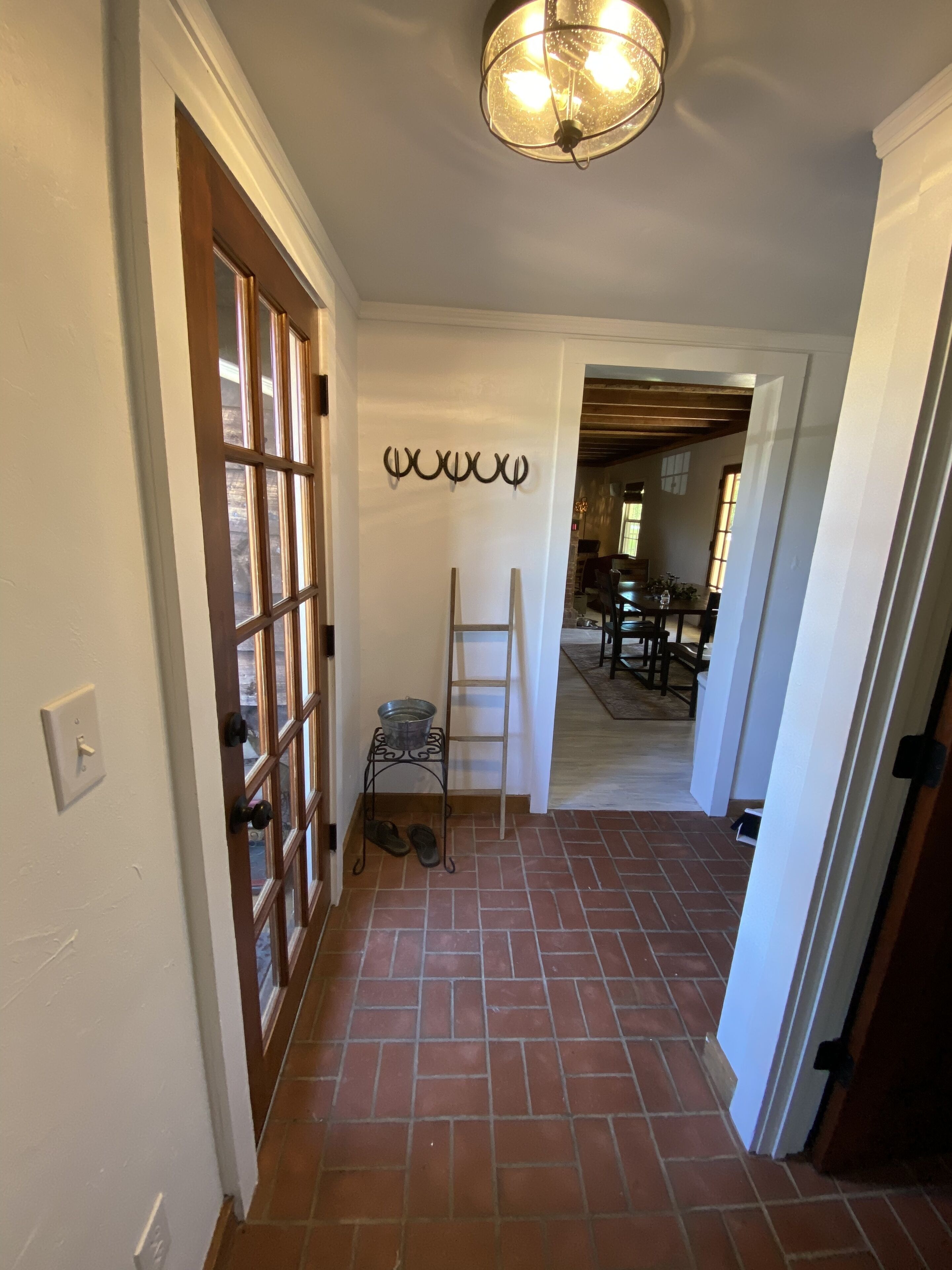 A hallway with a tiled floor, a wooden door with glass panels, a metal rack with a bucket, and a ladder leaning against the wall.