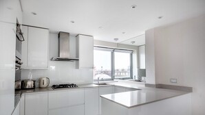 A modern kitchen with white cabinetry, a gas stove, a kettle, and a large window providing a city view. - Modern Chelsea 1BR w/ Balcony nr shops, by Blueground (London)