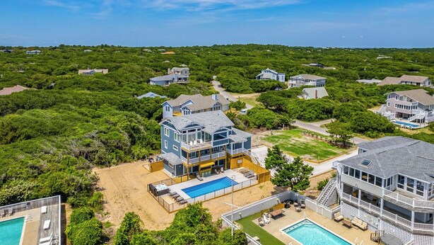 A large, multi-story house with a pool and a beach area.