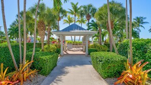 A covered walkway leading to a pavilion surrounded by palm trees and well-maintained hedges. - Renovated Anglers Reef 2BR + Sleeper + Ocean Views, Pool, Marina, Sleeps 8 (Islamorada)
