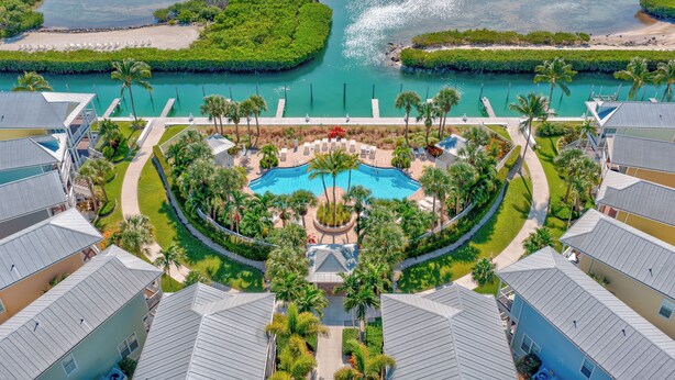 An aerial view of a resort with a central swimming pool, surrounded by lush greenery and palm trees, with a beach and water body in the background. - Renovated Anglers Reef 2BR + Sleeper + Ocean Views, Pool, Marina, Sleeps 8 (Islamorada)