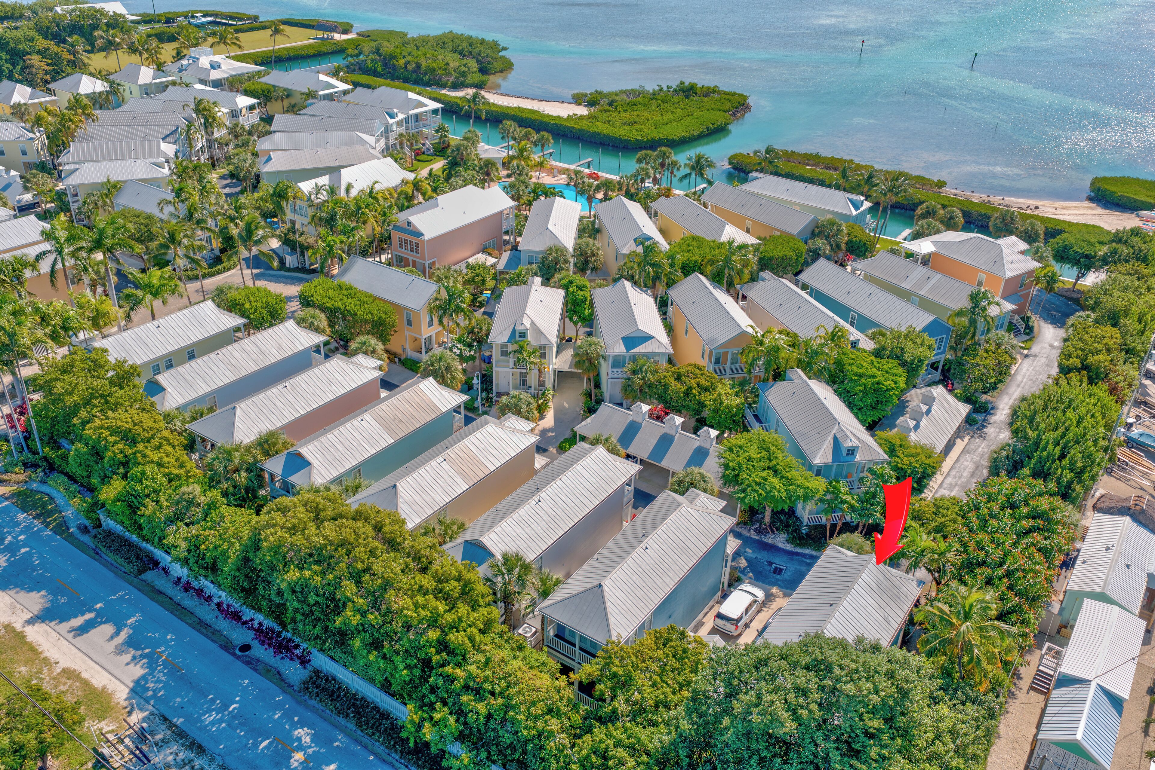 An aerial view of a coastal residential area with houses, a beach, and clear blue waters.
