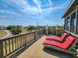 Un balcon doté de fauteuils de relaxation avec des coussins rouges, d’une balustrade en bois et offrant une vue sur les environs.