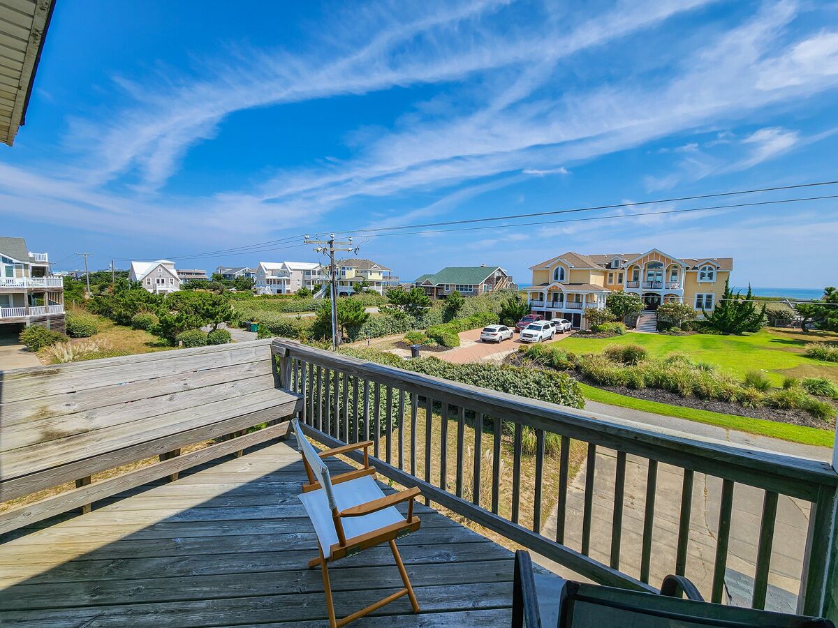 A wooden deck with a bench, overlooking a residential area with houses and a clear sky.