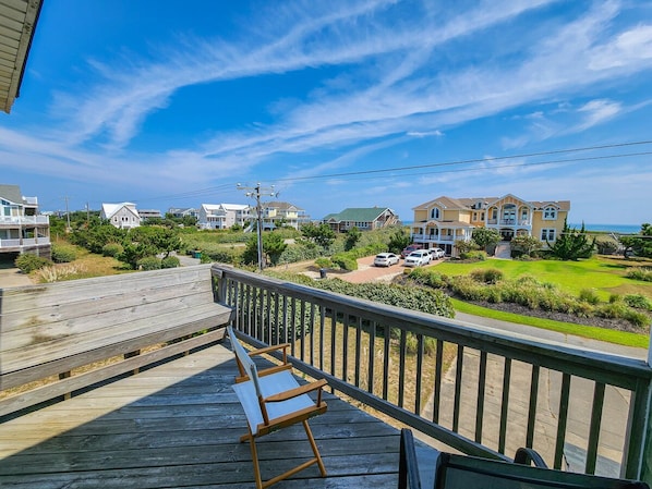 A wooden deck with a bench, overlooking a residential area with houses and a clear sky.