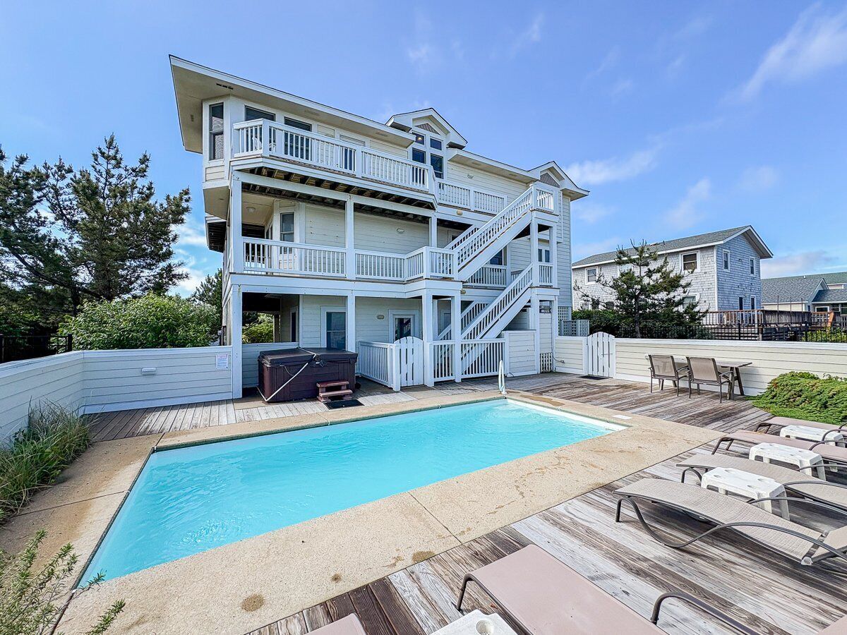 A two-story house with a swimming pool, a deck, and outdoor furniture.
