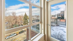 Blick aus einem Fenster mit mehreren Scheiben auf einen Parkplatz und eine verschneite Straße, im Hintergrund Gebäude und Bäume.