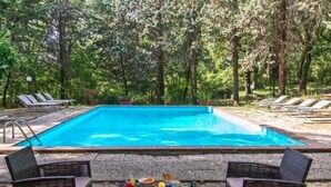 Une piscine rectangulaire à l’eau d’un bleu limpide, entourée de chaises longues et d’une table où sont disposées des boissons et des collations.