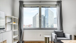 Una habitación moderna y luminosa con un ventanal grande, un sofá gris, una mesita redonda y una estantería empotrada.