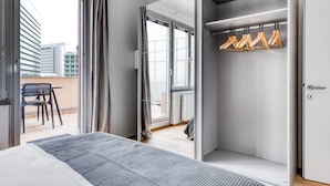 Una habitación de hotel moderna con una cama grande, un balcón con una silla y un armario con perchas de madera.