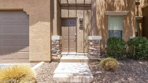 A residential building with a beige stucco exterior, a front door with a small overhang, a garage door, and a small front yard with a cactus and shrubs. - Cozy condo in Litchfield Park (Litchfield Park)